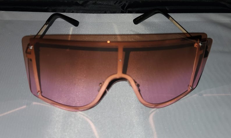 May include: Oversized sunglasses with a gradient pink lens and a black frame.