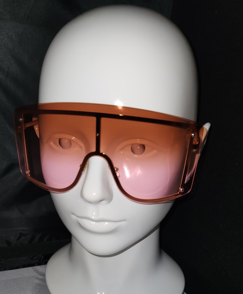 May include: A pair of oversized sunglasses with a brown to pink gradient lens. The sunglasses have a thick, square frame.