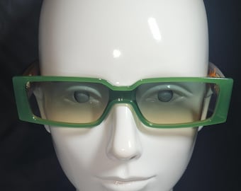Könnte beinhalten: Grüne rechteckige Sonnenbrille mit Verlaufsglas. Die Sonnenbrille sitzt auf einem weißen Mannequin-Kopf.