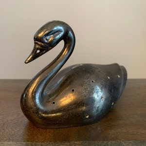 Puede incluir: Un infusor de té de plata con forma de cisne con una cabeza detallada y agujeros en todo el cuerpo.