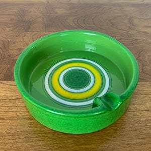 Op de afbeelding: Groene asbak van keramiek met een concentrisch cirkelontwerp in geel en wit.