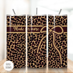 May include: A set of three stainless steel tumblers with lids and straws. The tumblers feature a brown and tan leopard print design. A burgundy band with the words "Made for more" is printed on the tumblers. A hand-drawn bow graphic is also featured.