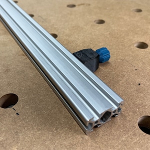 Könnte beinhalten: Eine silberne Aluminium-Extrusion mit einem schwarzen Kunststoffverbinder. Die Extrusion hat ein T-Nuten-Design und wird häufig im Holzhandwerk und anderen DIY-Projekten verwendet.