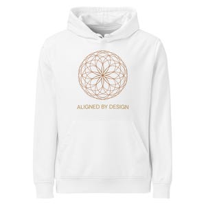 May include: White hoodie with a brown geometric design on the front. The design is a circular pattern with the text "ALIGNED BY DESIGN" below it. The hoodie has a front pocket and a hood.