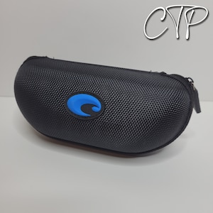 Op de afbeelding: Zwarte, ovale brillenkoker met een gestructureerd oppervlak. De koker heeft een blauw en zwart logo aan de voorkant en een ritssluiting. De koker is ontworpen om een bril te beschermen.