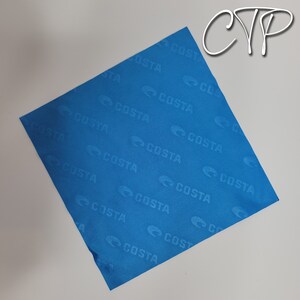 May include: A square, bright blue cloth with the word "COSTA" repeatedly printed across the surface. The logo is a stylized "C" shape. The cloth is slightly wrinkled and appears to be made of a soft material. The letters "CYP" are in the upper right corner.