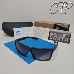 Op de afbeelding: Zwarte Costa zonnebril met een rechthoekig montuur, op een blauwe microvezeldoek. De zonnebril wordt geleverd met een zwarte etui, een kartonnen doos en informatiekaarten. De glazen hebben een gradi&euml;nt tint.