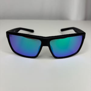 May include: Black sunglasses with rectangular frames and mirrored lenses that reflect blue and green hues. The sunglasses have a modern, sporty design, suitable for outdoor activities. The frames are thick and sturdy.