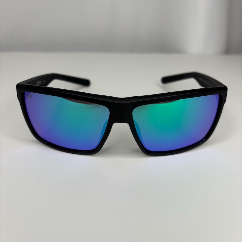 May include: Black sunglasses with rectangular frames and mirrored lenses that reflect blue and green hues. The sunglasses have a modern, sporty design, suitable for outdoor activities. The frames are thick and sturdy.