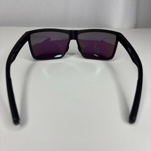 May include: Black sunglasses with rectangular frames and purple-tinted lenses. The sunglasses have a matte finish and a sleek, modern design. The arms of the sunglasses are curved for a comfortable fit.