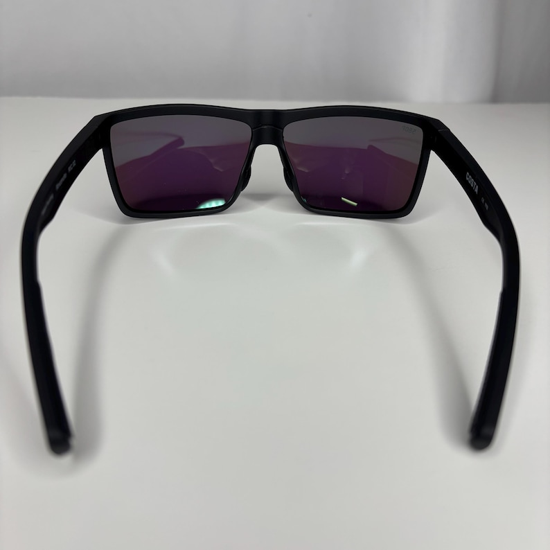 May include: Black sunglasses with rectangular frames and purple-tinted lenses. The sunglasses have a matte finish and a sleek, modern design. The arms of the sunglasses are curved for a comfortable fit.