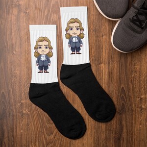 Könnte beinhalten: Ein Paar weiße Socken mit einem schwarzen Cartoon-Bild eines Mannes mit langen braunen Haaren, der einen Anzug und einen weißen Kragen trägt. Die Socken haben schwarze Bündchen.