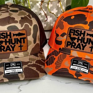 May include: Two trucker hats with camouflage patterns. One hat is brown and tan, the other is orange and brown. Each hat has a patch with the words "FISH HUNT PRAY" and a fish, bird, and cross graphic.