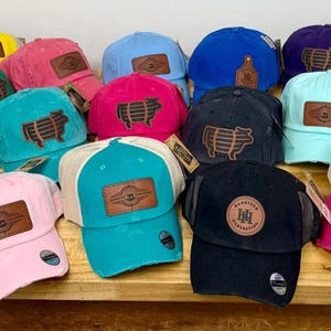 May include: A collection of 14 different baseball caps with various colors and designs. Some caps feature a pig design, while others have a logo with the letters "HH".