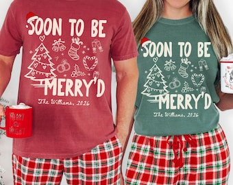 May include: A red t-shirt and a green t-shirt, both featuring the white text SOON TO BE MERRY'D, a Santa hat, a Christmas tree, bells, a stocking, rings, and candy canes. Below the text is The Williams, 2026. Both shirts are paired with red and white plaid pajama pants.