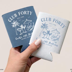 May include: Two can coolers, one blue and one white, are held in a hand. The coolers feature a beach-themed design with palm trees, cocktails, and the text "CLUB FORTY EST. 1986" and "Emily's 40th Birthday, Miami, Florida."