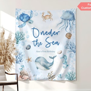 May include: A white fabric banner with an "Under the Sea" theme, featuring watercolour illustrations of a turtle, crab, jellyfish, and whale. The banner includes the text "Oneder the Sea" and "Alex's First Birthday".