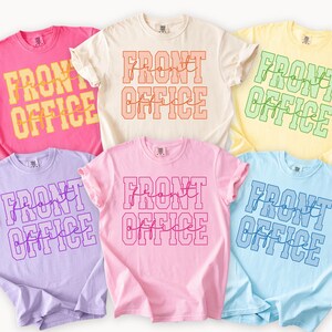 Può includere: Sei magliette a maniche corte con girocollo in vari colori pastello, tra cui rosa, crema, giallo, lavanda, rosa chiaro e azzurro. Ogni maglietta presenta la scritta FRONT OFFICE stampata in un carattere in grassetto con una sovrapposizione in corsivo.
