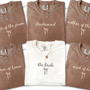 Personalized wedding party shirts arranged as a group showing honor roles and family titles. A stylish choice for engagement celebrations and wedding prep photos.
