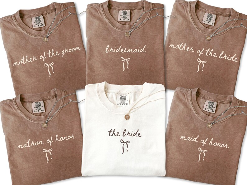 Personalized wedding party shirts arranged as a group showing honor roles and family titles. A stylish choice for engagement celebrations and wedding prep photos.