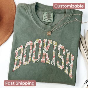 May include: A green t-shirt with a floral print design that says "BOOKISH" in a white outline. The shirt is made of a soft, comfortable material.