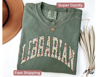 May include: A green t-shirt with a floral print design that reads "LIBRARIAN" in a white outline. The shirt is made of a soft, comfortable fabric and has a relaxed fit.