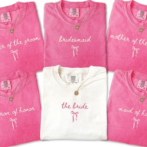 Matching Comfort Colors bridal party tees folded together with script lettering and bow detail. Ideal for bachelorette weekends and bridal party proposal gifts.