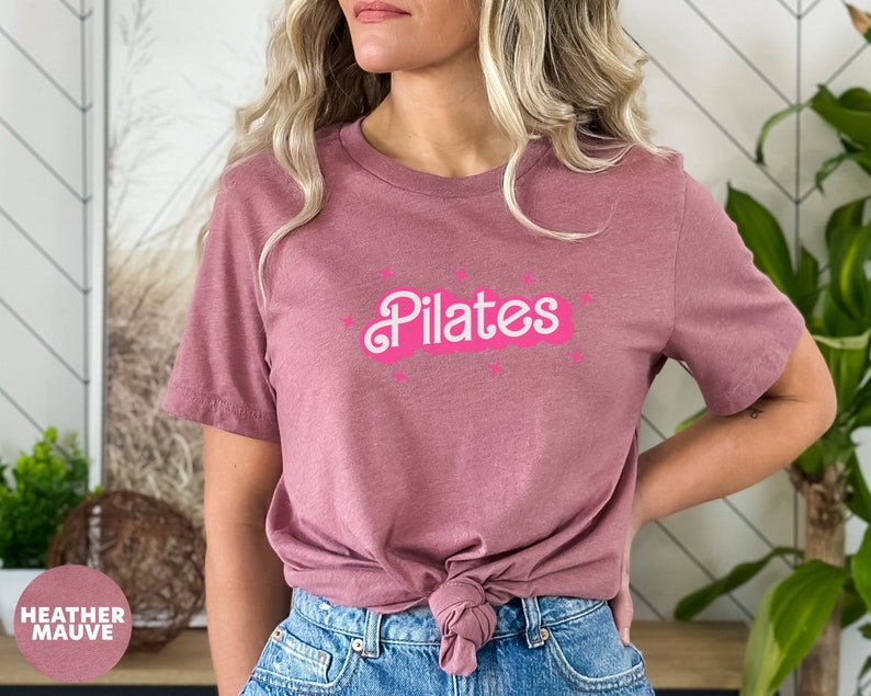 May include: A heather mauve t-shirt with the word "Pilates" in white text on a pink cloud graphic.
