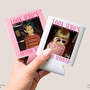 May include: Two foam can coolers, one light pink and one white, each featuring a childhood photograph and the printed text "LOOK WHO'S GETTING MARRIED" in bold pink lettering. The white cooler also includes the name "Emily" in a script font.