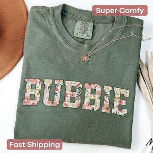 May include: A green t-shirt with a floral print spelling out the word "BUBBIE".