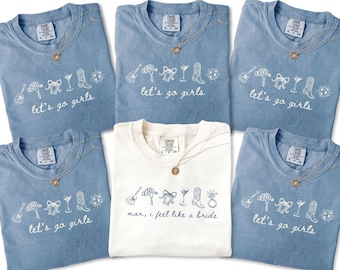 May include: A collection of blue and white t-shirts with the phrases "let's go girls" and "man, I feel like a bride" printed on them. Each shirt features a necklace and a line drawing of a guitar, bow, martini glass, cowboy boot, and disco ball.