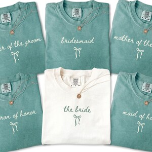 Flat lay of bridal party shirts featuring maid of honor matron of honor bridesmaid and mother roles. Designed for coordinated getting ready outfits on the wedding morning.