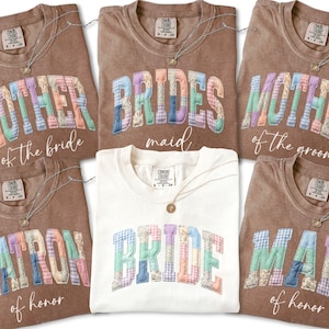 May include: Several Comfort Colors t-shirts in different shades, each with a wedding role printed on it. The text includes "Mother of the Bride," "Bridesmaid," "Mother of the Groom," "Matron of Honour," and "Bride." Each shirt has a patchwork design.
