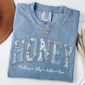 May include: A pale blue Comfort Colors t-shirt featuring the word "HONEY" in a patchwork design. The letters are decorated with floral and gingham patterns. Below the word are the names Mallory, Jilly, Addie, and Liam.