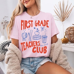 Personalized teacher graphic tee featuring First Grade Teachers Club wording with apple, books, globe, and pencil design. This educator shirt is perfect for elementary teachers who want a cheerful and welcoming school look.