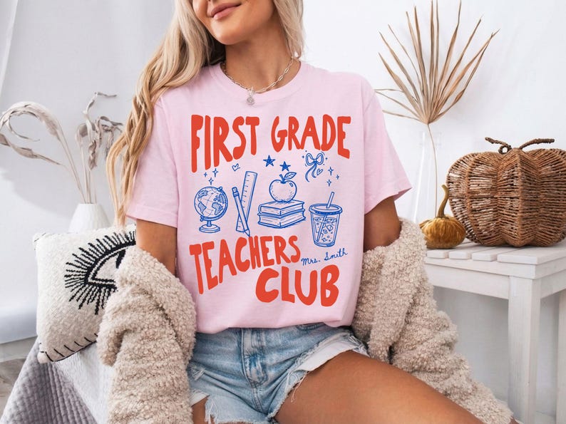 Personalized teacher graphic tee featuring First Grade Teachers Club wording with apple, books, globe, and pencil design. This educator shirt is perfect for elementary teachers who want a cheerful and welcoming school look.