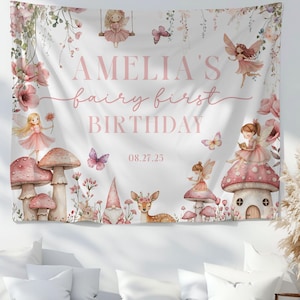 May include: A white tapestry with a fairy theme, featuring illustrations of fairies, mushrooms, butterflies, and flowers. The text "AMELIA'S fairy first BIRTHDAY" is displayed in pink. The date "08.27.25" is also visible.