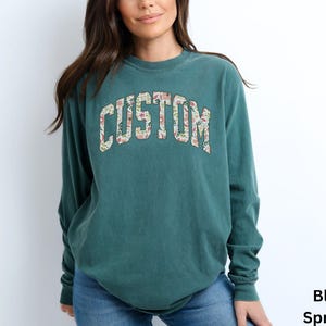 Ideal as a thoughtful and personalized gift, this long sleeve custom t-shirt lets you create a unique message with its floral college letter design.