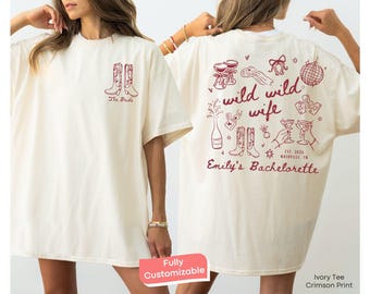 Puede incluir: Camiseta color marfil con estampado carmesí. La parte delantera presenta botas de vaquero y el texto "The Bride". La parte trasera muestra las palabras "wild wild wife" con ilustraciones de champán, botas y anillos. También se ve el texto "Emily's Bachelorette".