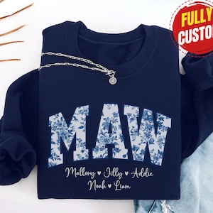 May include: Navy blue sweatshirt featuring the word "MAW" in a floral pattern. The names Mallory, Jilly, Addie, Noah, and Liam are printed below. A silver necklace with a pendant is draped across the sweatshirt.