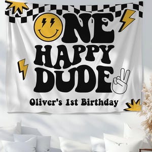 May include: White fabric banner with the text "ONE HAPPY DUDE" in black, with a smiley face and lightning bolt graphics. The banner also includes the text "Oliver's 1st Birthday". A black and white checkered pattern is at the top.