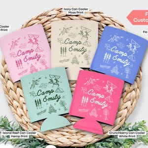 May include: Five different color can coolers with a camping theme. The coolers are all personalized with the text "Camp Emily". The colors are pink, blue, green, ivory, and white.