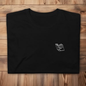 May include: Black t-shirt with a white outline of an open book embroidered on the front.