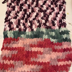 May include: A multi-colored knitted throw blanket with a pink, red, green, and purple color scheme. The blanket is made with a chunky yarn and has a soft, fluffy texture.