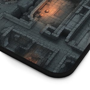May include: A rectangular desk mat featuring a top-down isometric view of a dark stone dungeon map. The design includes gray cracked stone walls, tiled floors, and small glowing orange light sources illuminating specific areas of the layout.