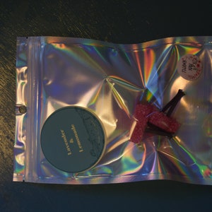 May include: A silver iridescent resealable bag with a round teal sticker that says "Lavender & Lemonade" and a pink and black candy cane. The bag also has a small pink sticker that says "Thank You".