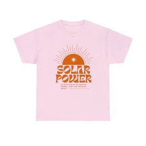 Könnte beinhalten: Hellrosa T-Shirt mit orangefarbenem Aufdruck "SOLAR POWER" und einem Sonnensymbol. Darunter steht der Satz "WE CAN GO LOOK AT THE SUNRISE BY EUPHORIA, MIXED WITH EXISTENTIAL VERTIGO."