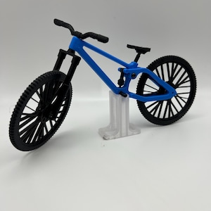 May include: A blue and black mountain bike model with a black stand. The bike has a suspension fork and a rear shock.