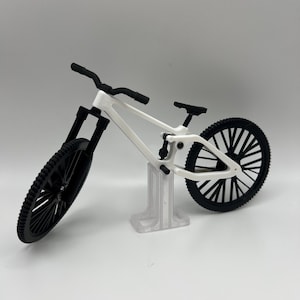 May include: A white miniature mountain bike with black wheels and a black handlebar. The bike is on a clear plastic stand.