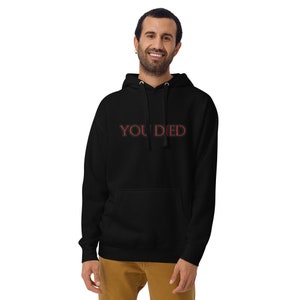 May include: Black hooded sweatshirt featuring the red text "YOU DIED". The garment has a front pocket and a drawstring hood. The person wearing the sweatshirt is smiling.